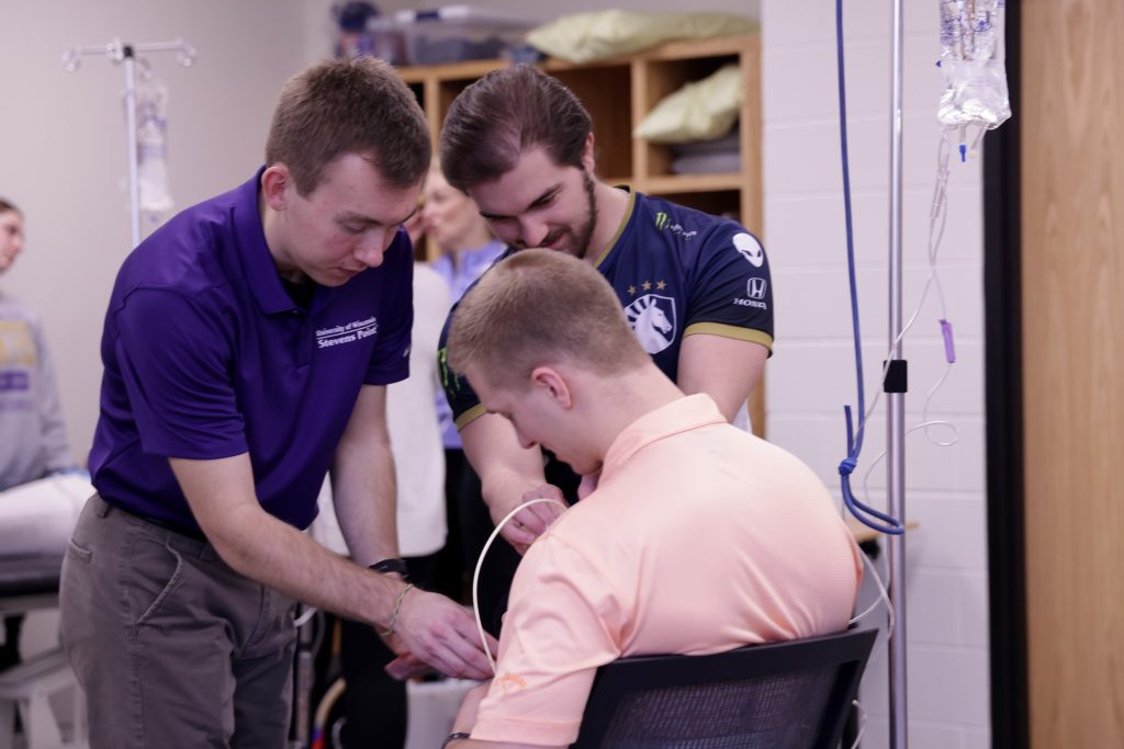 Two students assisting another in a chair in a health care setting.