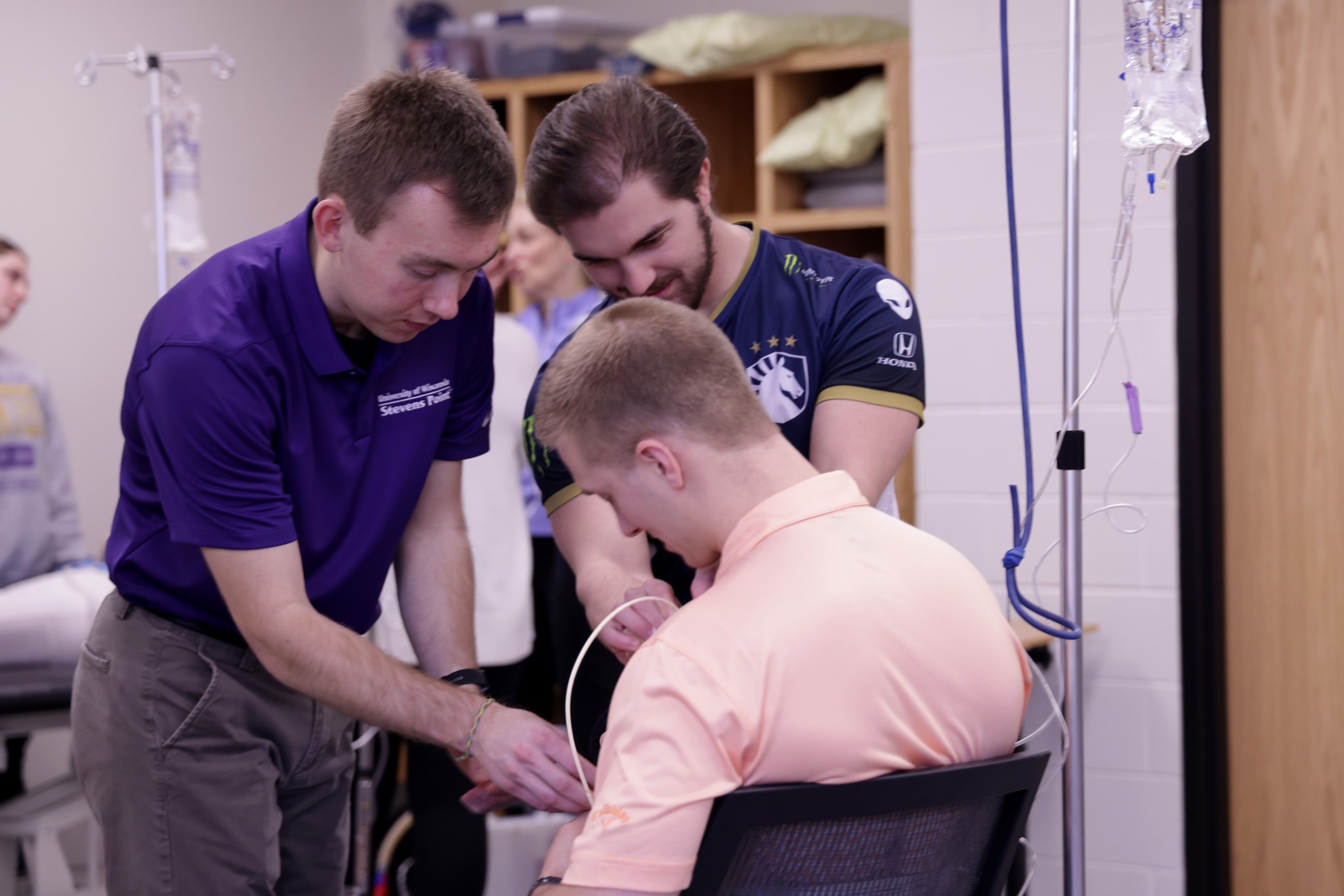 Two students assisting another in a chair in a health care setting.