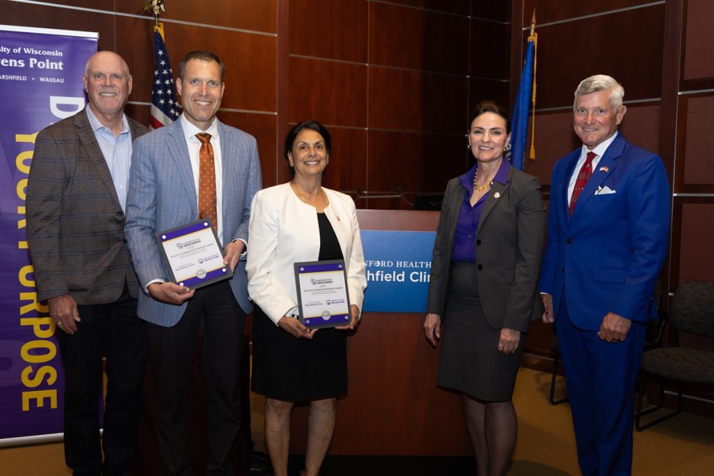 Group of five leaders from university and healthcare partners holding awards during ceremony.