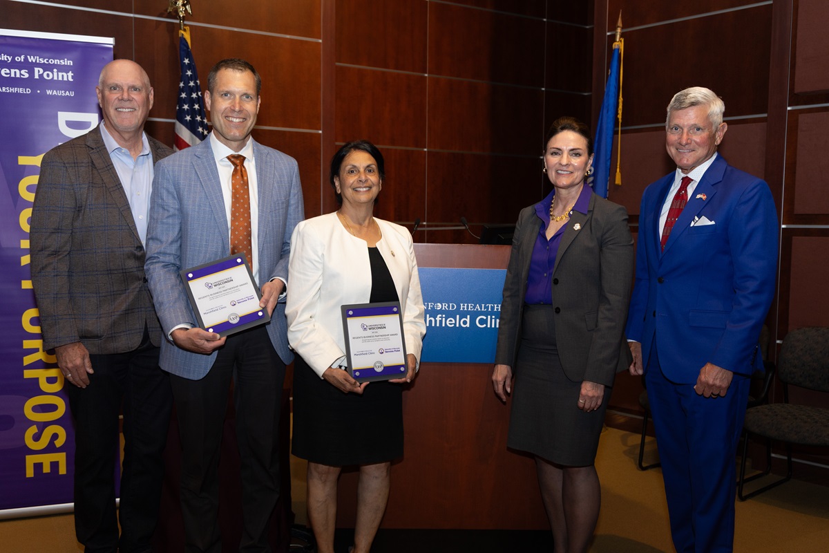 Group of five leaders from university and healthcare partners holding awards during ceremony.