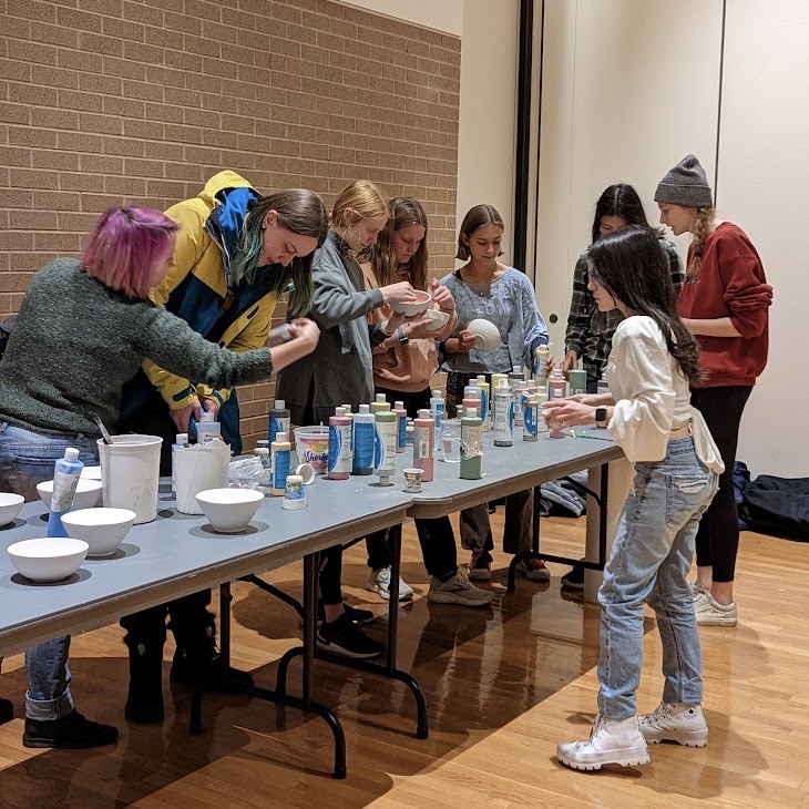 Students standing around a table painting bowls.