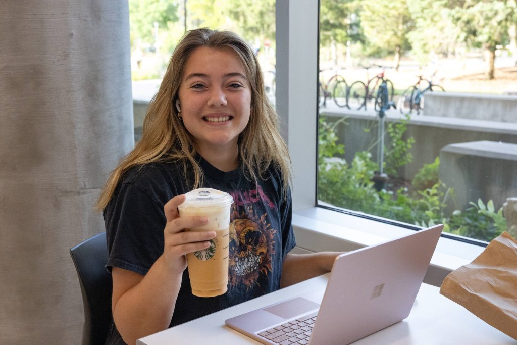 Student holding an iced coffee with laptop open